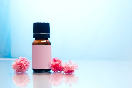 Bottle of essential oil with pink flowers on blue background.の写真素材