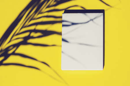 Top view of an open notebook and shadow from palm tree leaf on yellow background. Copy space.