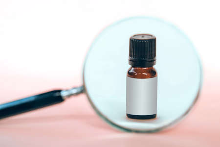 Bottle of essential oil under the magnifying glass on a pink background.