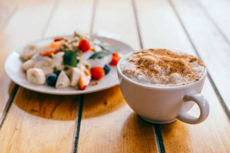 Plate with fruits and yogurt and cup of coffee on the wooden table on veranda. Breakfast outside in...