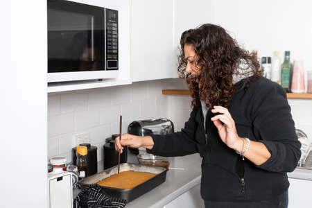 A woman is baking cake in a kitchen, checking if it is ready with a wooden stickの写真素材