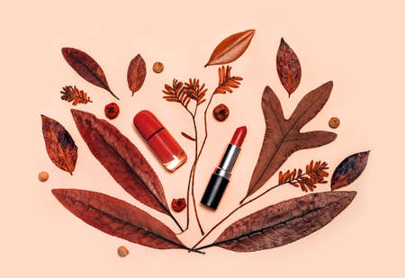 Decorative flat lay composition with cosmetics, woman beauty products, red lipstick, nail polish, decorated with autumn leaves and berries. Flat lay, top view on light background, fashion still lifeの写真素材