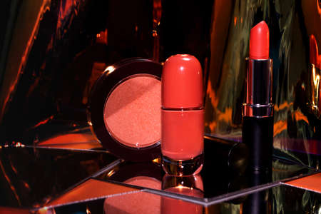 Open red lipstick, nail polsh and blush with mirror reflection on glass surface, shiny gold packages, luxury cosmetic accessory setの写真素材
