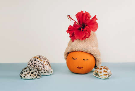 Pumpkin with painted face and facial mask, towel with flower and seashells on pastel blue background. Spa concept, Helloween, Copy space.の写真素材