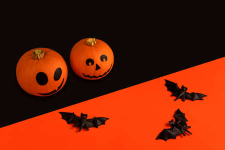 Little pumpkins with painted faces for Halloween and bats on orange and black backgroundの写真素材