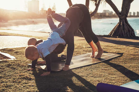 Young mother and two sons doing gymnastics and stretching in the city park on sunset with ocean...