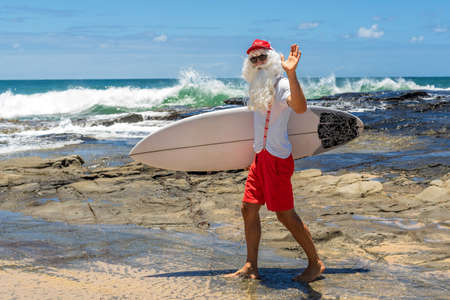 Santa Claus with a surf board with the ocean on backgraund. Australia, Christmas in summer time.の写真素材