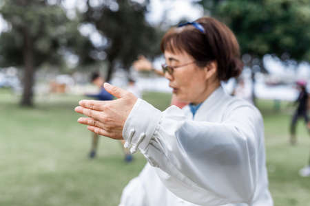 Mature chinese woman do tai chi with blirred group of people outdoor in the parkの写真素材