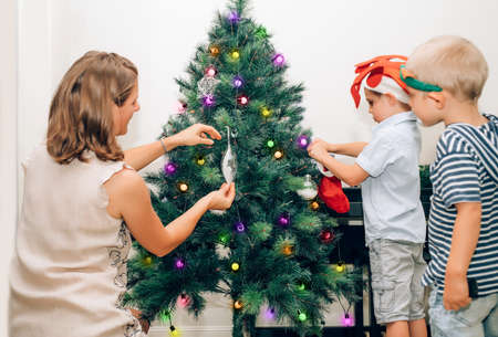 Mother with two little kids decorating Christmas tree.の写真素材