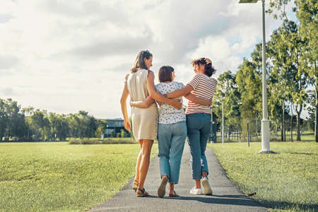 Three women friends with happiness emotion walking in the park hugging each otjher and smiling joyful.の写真素材