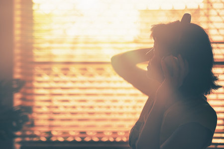 A silhouette of woman with Headphone or Headset on her head with the window and sunlight on background.の写真素材