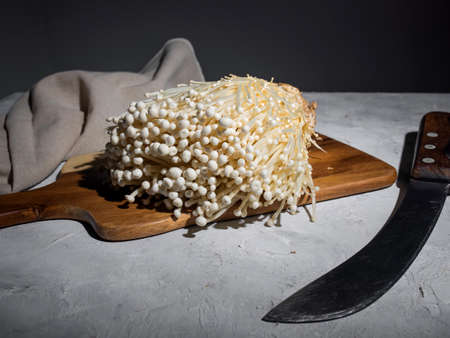 Fresh golden needle mushroom or enoki mushrooms, on wooden cutting board with vintage knife on gray concrete backgroundの写真素材