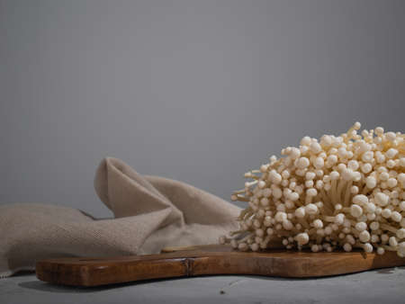 Fresh golden needle mushroom or enoki mushrooms, on wooden cutting board on gray concrete backgroundの写真素材