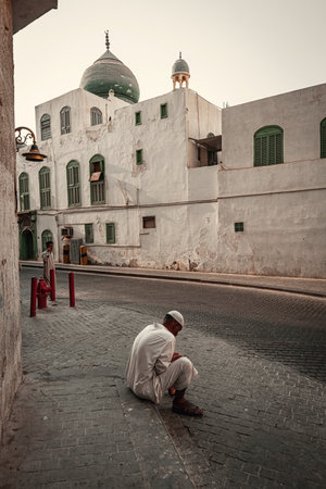 Muslim man sitting on the pavement next to Old building of Al Falah school in Jeddah old town Saudi...