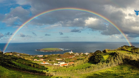 Breathtaking view of the amall village and lighthouse at SÃ£o Jorge island in Azores with huge rainbow in the sky Portugalの写真素材