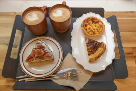 Two cups of coffee, cheese cake and figs tart on the tray in coffee shopの写真素材
