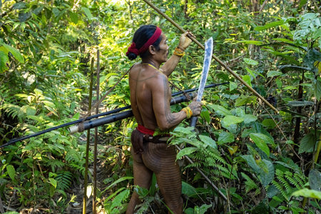 Mentawai shaman wearing traditional attire and body decorations hunting in the jungle with a...