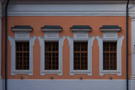 Windows in white frames with bars on the orange wall of an ancient building. Vintage. Ancient architecture. Story. Designの写真素材