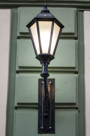 Photo of a street design. A vintage electric lamp on one of the buildings resembles an old lamp with a lamp inside. Green, beige, light, lightingの写真素材