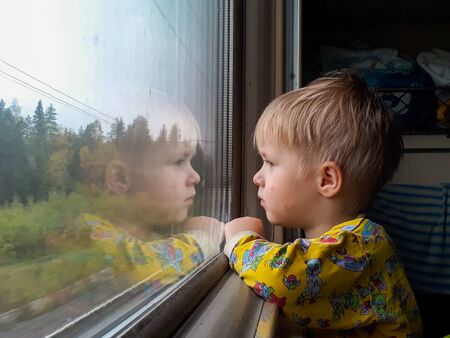 A little blond-haired boy of three years rides on a train, eats candy and looks out the window,...