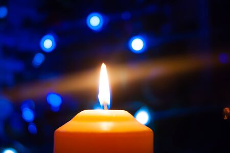 A burning orange candle on a dark background with blue lights - a Christmas New Years eve divination...