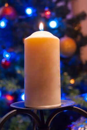 A large candle burns against the background of a garland with shining lights. Vertical photo, defocus. Mystic esoteric romance divination mood christening Christmas carol setcersの写真素材
