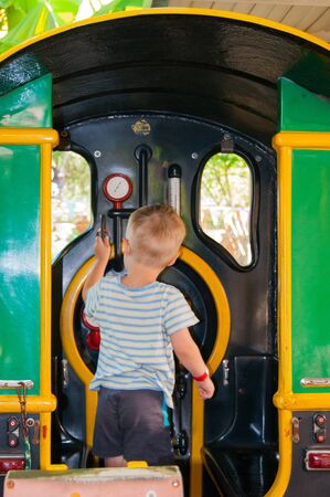 A little boy of three years rides in a children's train in the Riviera amusement park, Sochi with his back to the viewer. Rest, tropics, rest, activation. Vertical photoの写真素材