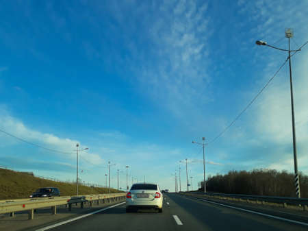 A road or highway leading to the horizon. View from the car window. Northern dim summer, blue sky with white clouds. Journey, the way home.のeditorial素材
