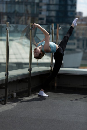 A teenage girl in a blue sports top and black leggings on a terrace among skyscrapers
