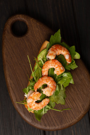 Bruschetta on a fresh baguette with arugula, cream cheese, avocado and shrimp on a wooden boardの写真素材