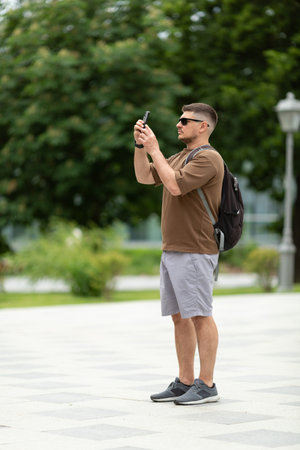 A male tourist in sunglasses takes pictures of the sights on his phone