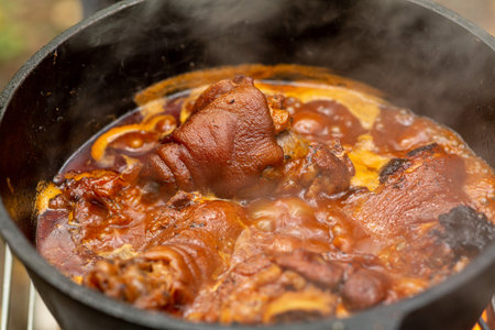 Pork knuckle languishes in sauce in a cauldron over a fireの写真素材