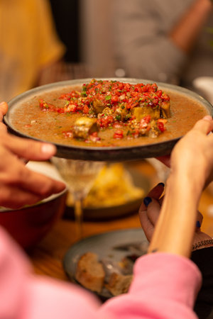 A plate with an eggplant snack with tomatoes is passed from hand to handの写真素材