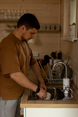 A man washes a mug in the sink under running waterの写真素材