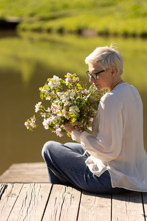 A beautiful mature white woman with short hair and glasses with a bouquet of apple blossomsの写真素材
