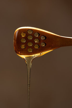 Fresh floral honey drips from a wooden spoon, close-up