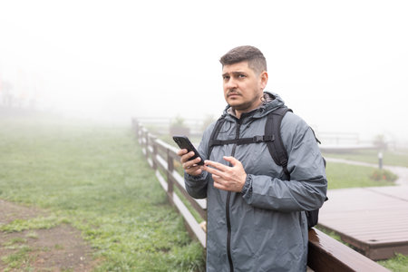 A puzzled man looks at information on his phone on a foggy dayの写真素材