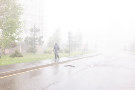 A man walks through a foggy city along an empty roadの写真素材