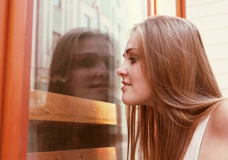 Curious Young Woman Looking Through Window Outdoorsの写真素材