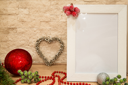 Christmas mock up. White frame with red and silver christmas ball, red and green berries covered with snow, fir tree branches, red beads decorations on brick wall background. Copy space.の写真素材