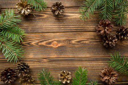 FIr branches and golden pine cones frame on brown wooden table background. Top view. Free space for...