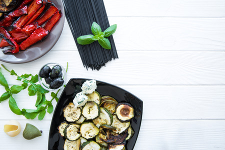 Italian cuisine, grilled vegetables and raw black pasta on white wooden rustic table. Space for text. Copy space.の写真素材