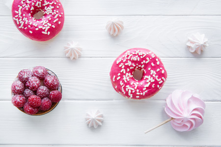 Bright pink doughnut and raspberry tart cake on white table backround, top view. Little and big meringues.の写真素材
