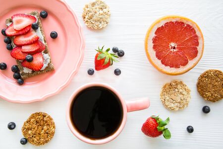 A cup of coffee and heathy snacks, sandwich with strawberry, blueberry and oat cookies on white...