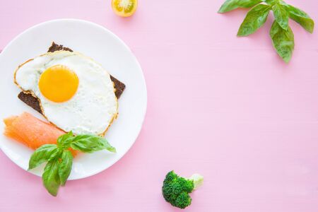 Fried eggs with smoked salmon, fresh basil leaves, broccoli and rye bread on bright colorful pink backgroud.の写真素材