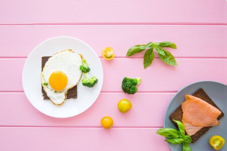 Delicious eggs with smoked salmon toasts with vegetables and greens on wooden pink background, top...