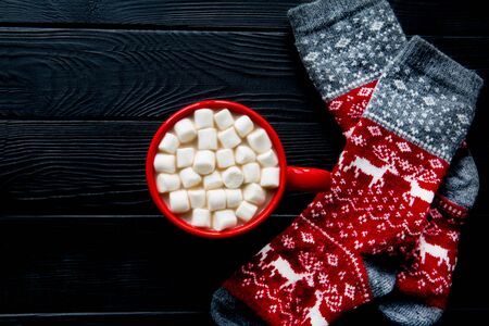 Winter hot beverage with marshmallow and red christmas ornament socks with deer on wooden black rustic table background. Copy space, space for text.の写真素材