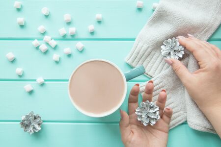 A cup of winter beverage with sweets and Christmas silver cones, turquoise table background, top...
