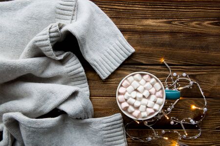 Tasty hot chocolate cup with marshmallow on rustic brown table, cozy winter background with Christmas yellow lights, top view.の写真素材