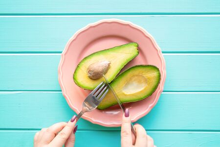 Female hands holding cutlery and cutting avocado. Diet concept. Colorful living coral plate on...